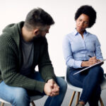 black-female-psychotherapist-taking-notes-while-talking-man-during-counselling